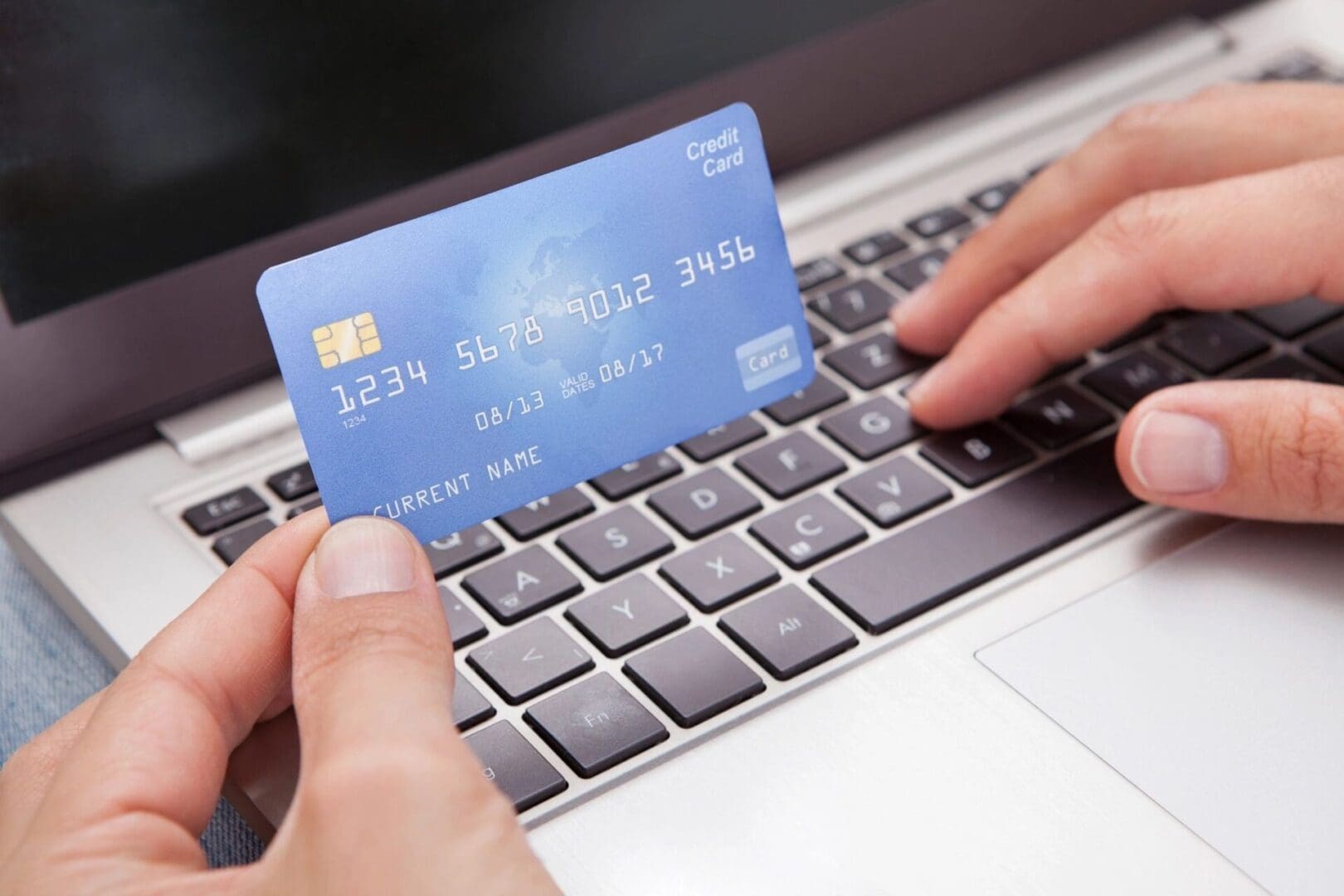 A person holding their credit card over the keyboard of a laptop.