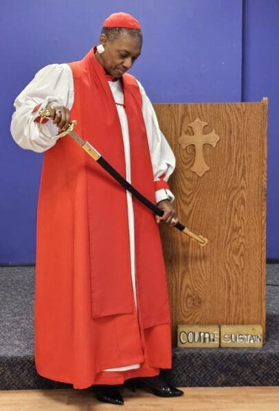 A man in red robe holding a wooden stick.